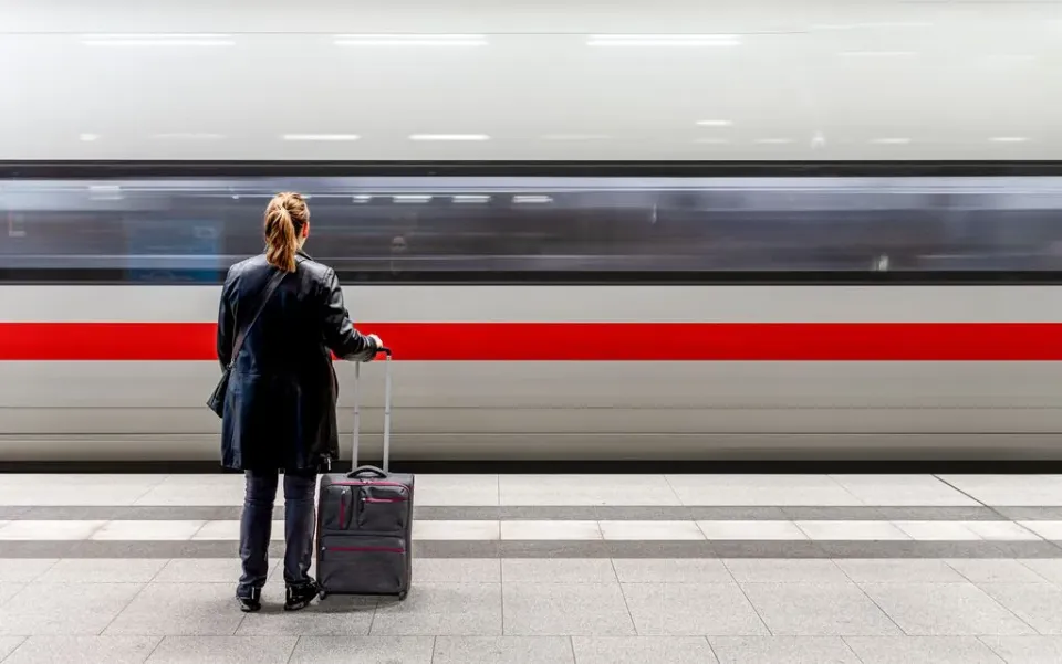 Eine Frau mit Koffer steht am Bahnsteig während ein ICE einfährt.