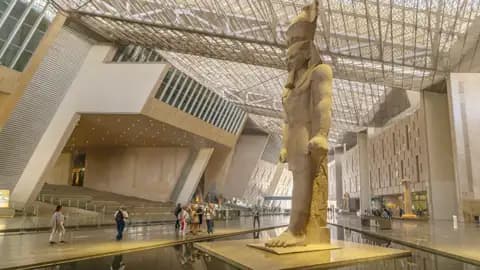 Reisende bestaunen die riesige Pharaonenstatue in der modernen, lichtdurchfluteten Halle des Grand Egyptian Museum in Kairo.